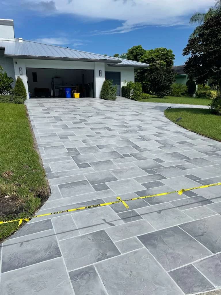 Concrete Magic crew member hand-applying decorative concrete overlay coating to a driveway in front of a Florida garage