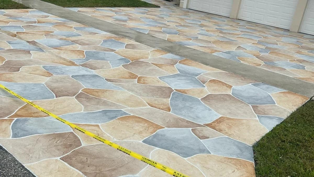 Multi-tone tan, gray, and blue flagstone stamped concrete driveway freshly finished with caution tape marking the curing area