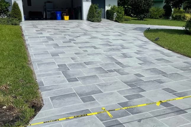 Freshly finished gray tile-pattern stamped concrete driveway with caution tape marking the curing area