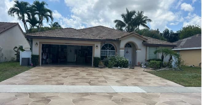 Completed tan flagstone stamped concrete driveway leading to a Florida home with tile roof and palm trees
