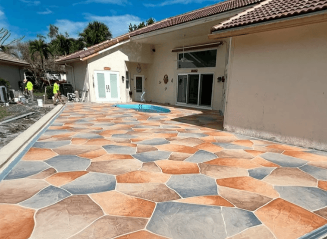 Florida patio with multi-tone decorative concrete overlay in orange, tan, and warm earth tones surrounding a pool enclosure
