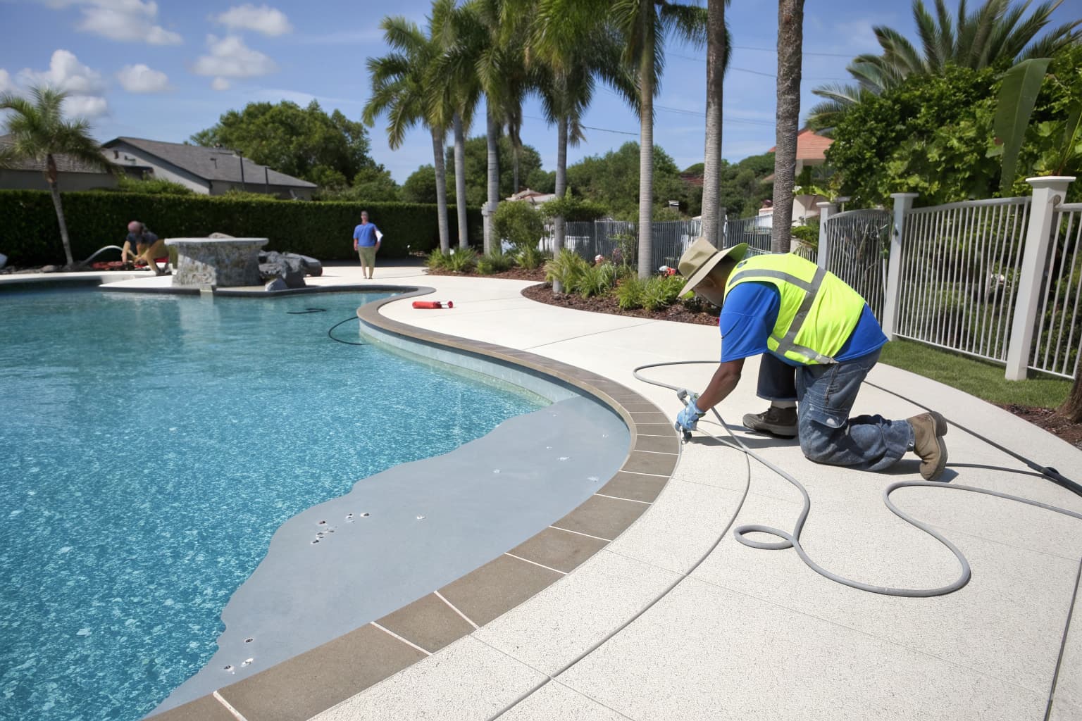 Contractor applying a spray-applied pool deck overlay coating around a Florida swimming pool