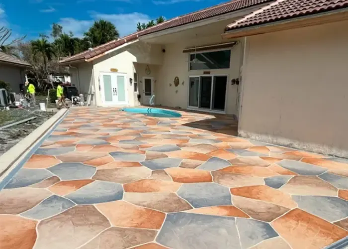 Colorful stamped concrete patio with irregular stone pattern in warm tones beside a stucco home with pool in Naples Florida