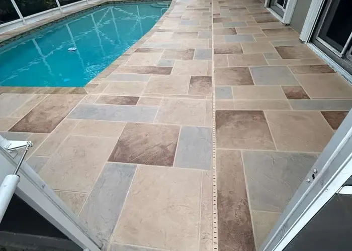 Screened-in backyard pool with wide tiled pool deck resurfaced in tan stone-look tiles in Naples Florida
